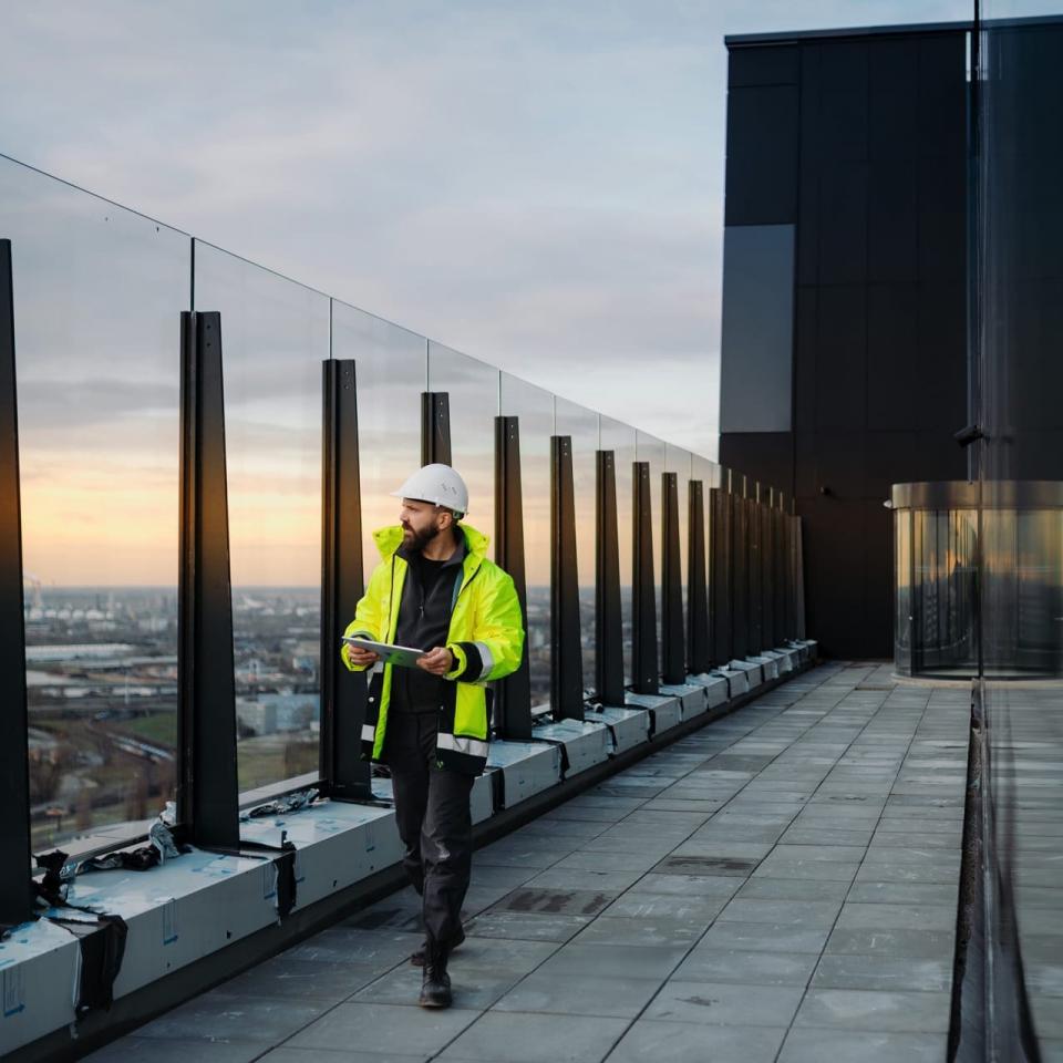 Bauingenieur mit Tablet bei Fassadeninspektion auf Hochhaus mit Glasfassade