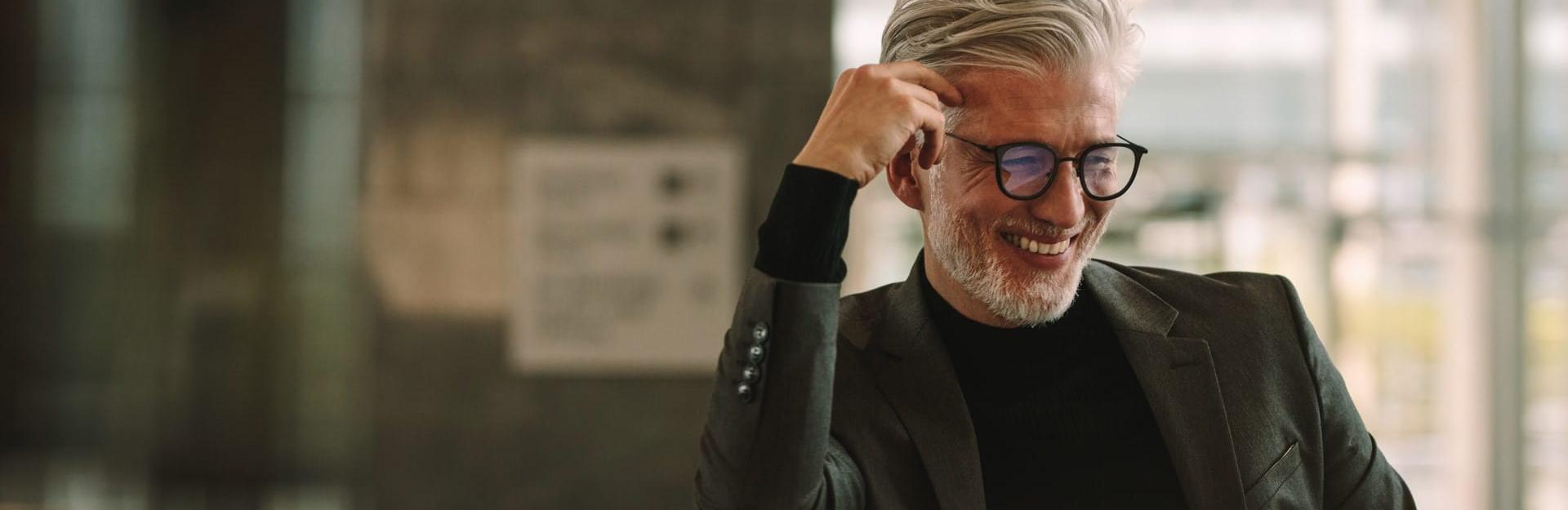 Freundlich lächelnder grauhaariger, aber dennoch sehr modern und jugendlich gebliebener, seriöser Mann mit Brille